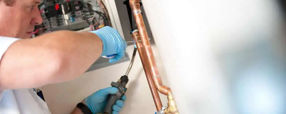 Water heater repair technician testing copper pipe connections and controls in Chico, CA